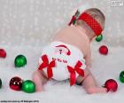 A baby very Christmas, with a diaper of Santa Claus and various colored balls